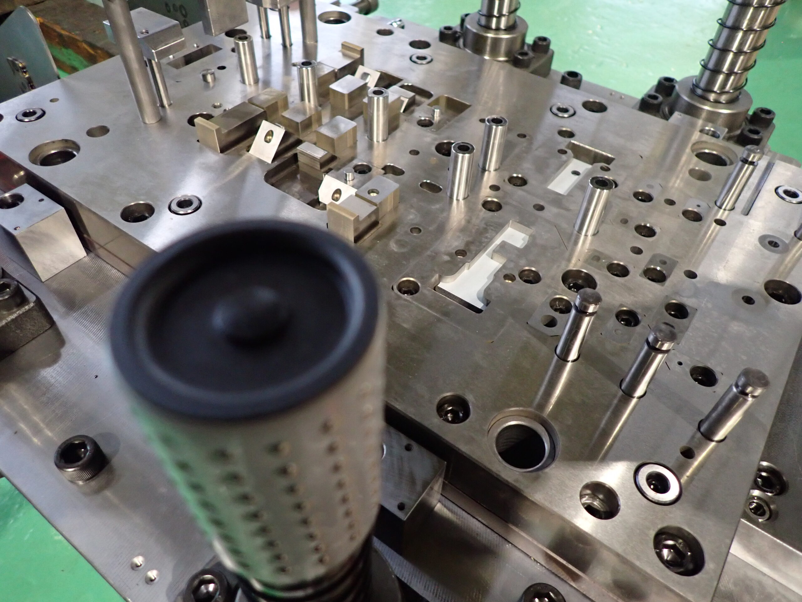 開かれた順送プレス金型の内部写真。現場でのメンテナンス（点検・調整）を高めるためにあえて細かく分割された入れ子構造や、負荷を分散させる工程レイアウトが見える。