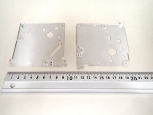 アルミ材A5052（t0.25mm）を用いた薄板カバー部品COVER BOTTOM。順送プレス金型内の工程バランス調整により、ドロー部の亀裂を抑えながら製品全体の高い平面度を両立させた加工サンプル。